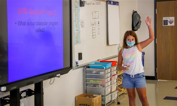 student stands in front of class next to Smartboard